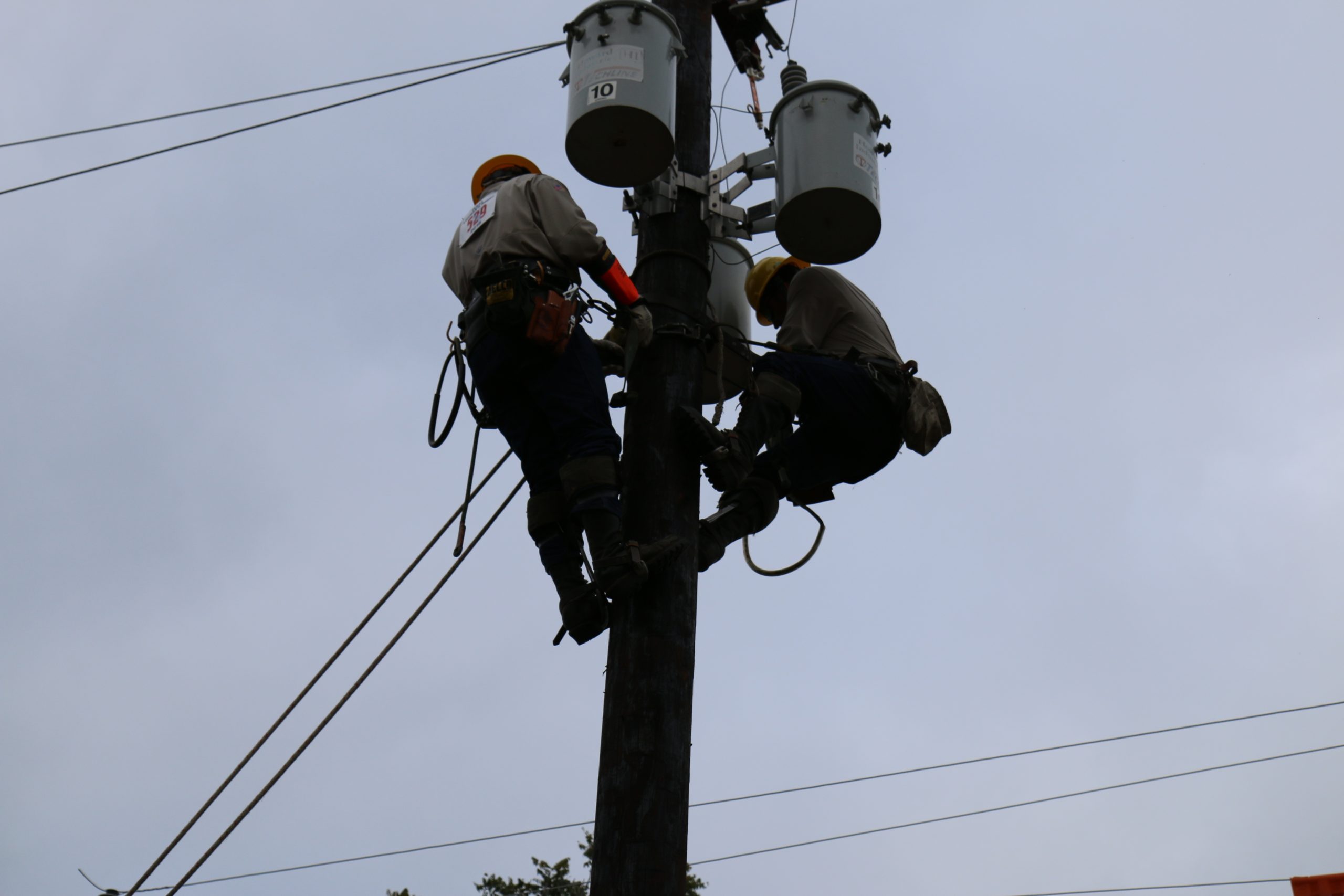Two GVEC linemen at the top of a pole, competing at the Texas Lineman's Rodeo
